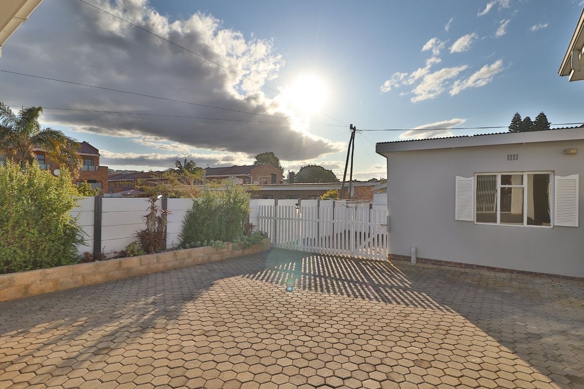 A paved rear courtyard area featuring a secure gate, boundary wall, and exterior wall with window shutters.