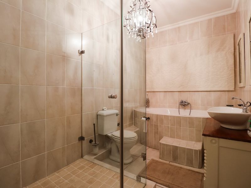 A well-maintained bathroom featuring a glass-enclosed shower, a built-in bathtub with a tiled step, and a vanity basin with neutral ceramic wall and floor tiles.