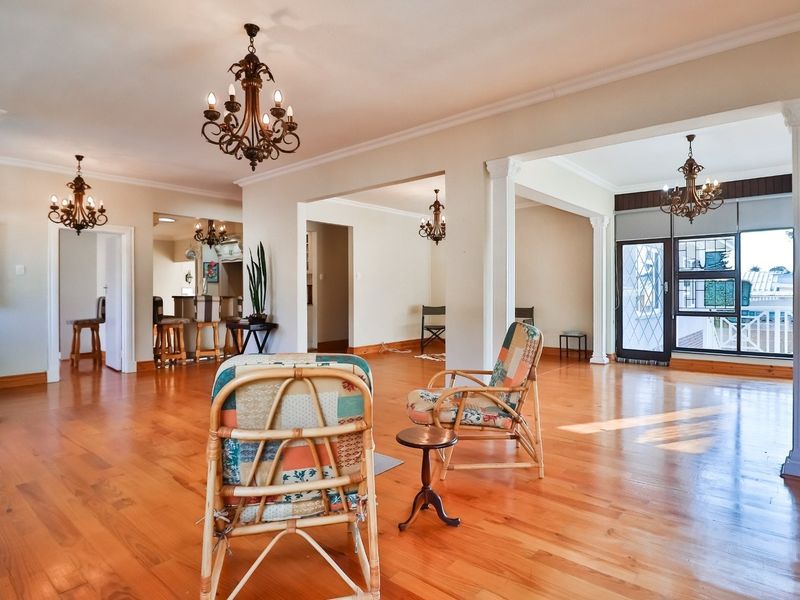 Spacious open-plan living area featuring polished hardwood flooring, decorative columns, and classic wrought iron chandeliers, offering a bright and versatile layout.