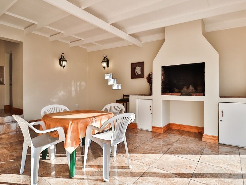 Covered patio area featuring a built-in braai, tiled flooring, and exposed beam ceiling, providing a functional space for outdoor entertaining.