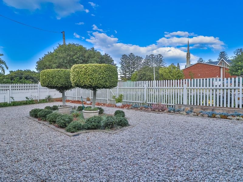 A well-maintained garden area featuring a gravel surface, manicured topiary trees, and a white picket fence boundary.