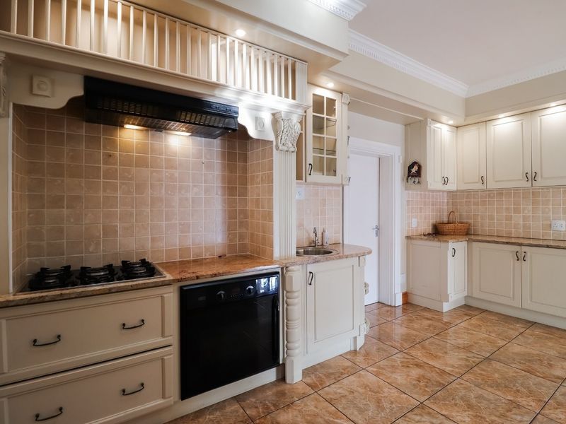 A traditional kitchen featuring cream cabinetry, granite countertops, a built-in oven with gas hob, and decorative architectural detailing.