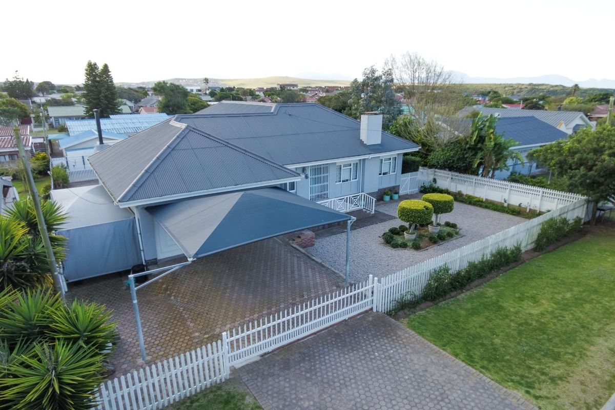 Aerial view of a well-maintained residential property featuring a metal roof, paved driveway with shade sail, and a neat gravel garden with picket fencing.