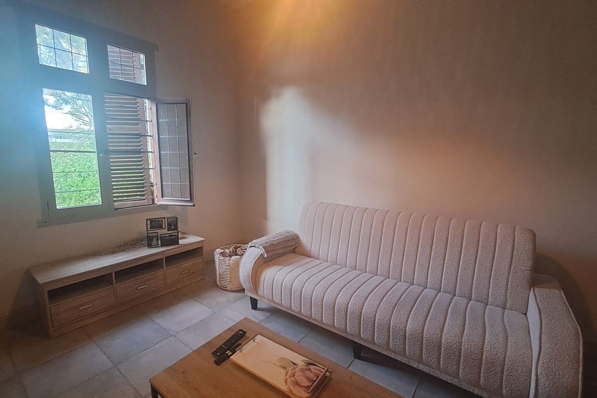 A living room featuring tiled flooring and a large casement window with shutters, providing natural light to the space.