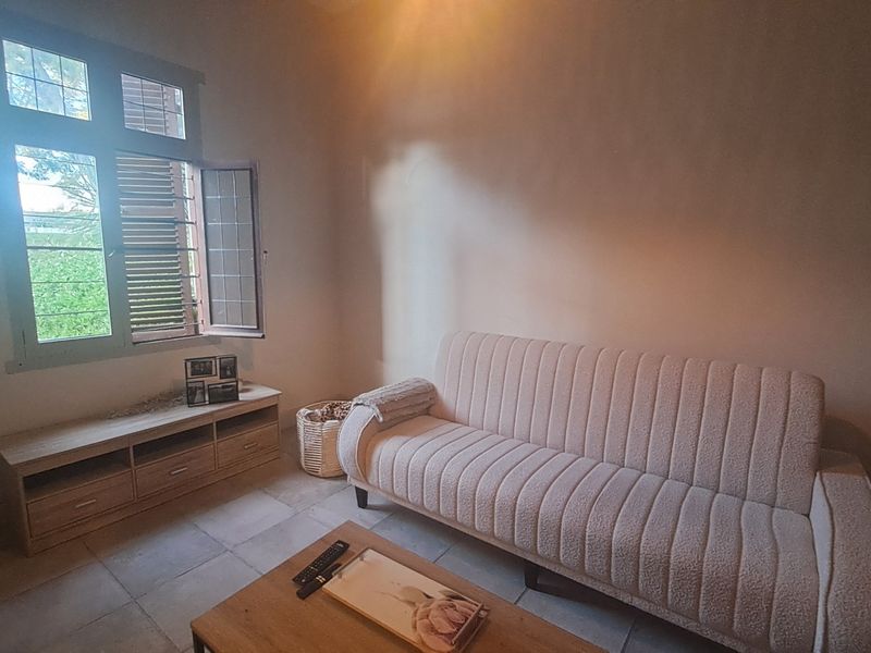 A living room featuring tiled flooring and a large casement window with shutters, providing natural light to the space.
