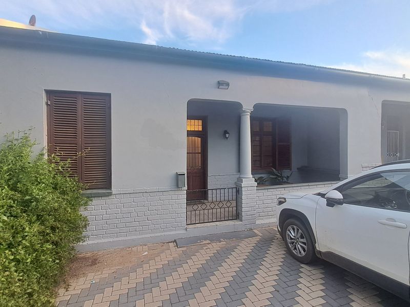 Front elevation of a house featuring a covered patio, brick facade, and timber shutters, with a paved driveway area.