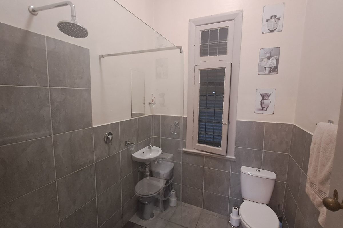 A compact bathroom featuring grey wall and floor tiles, a glass shower screen, a wall-mounted basin, and a standard toilet.
