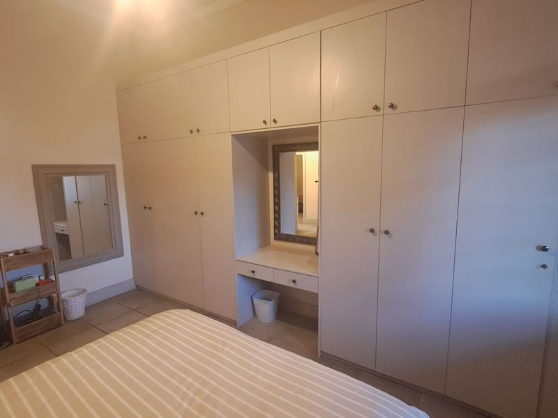 Bedroom featuring extensive floor-to-ceiling built-in cupboards with an integrated vanity station and neutral tiled flooring.