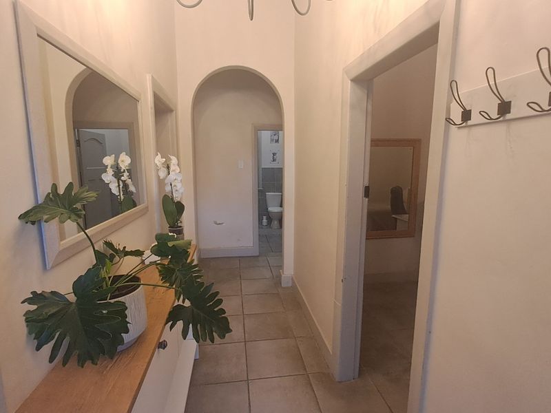 A bright hallway featuring tiled flooring, an arched architectural detail, and wall-mounted coat hooks, providing access to adjacent rooms.