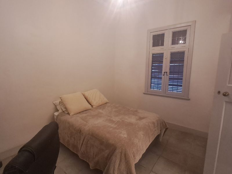 A simple bedroom featuring tiled flooring, a timber-framed window with integrated shutters, and a classic panel door.