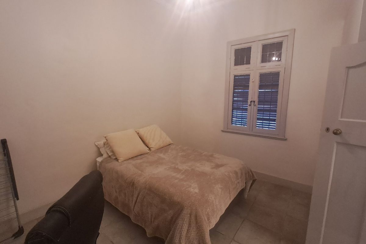 A simple bedroom featuring tiled flooring, a timber-framed window with integrated shutters, and a classic panel door.
