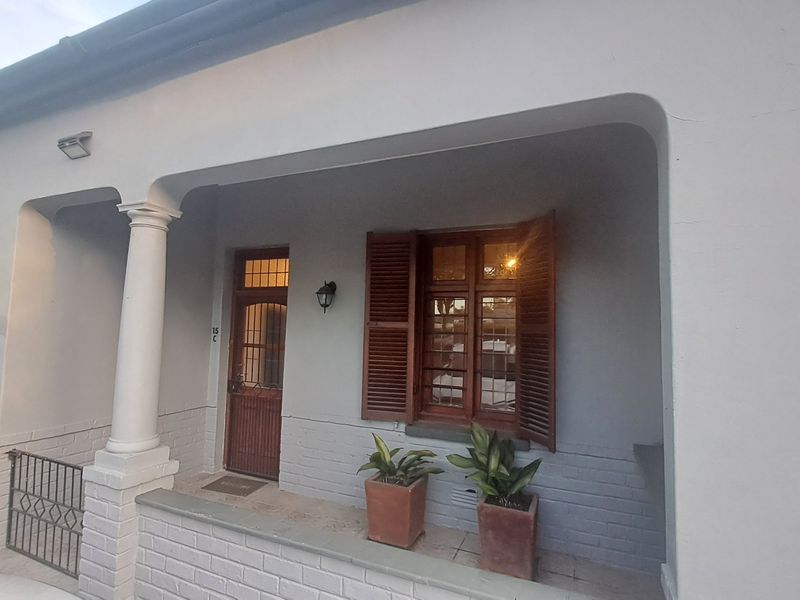 A charming front entrance featuring a covered porch, classical column, timber shutters, and a traditional timber-framed door with brickwork detailing.