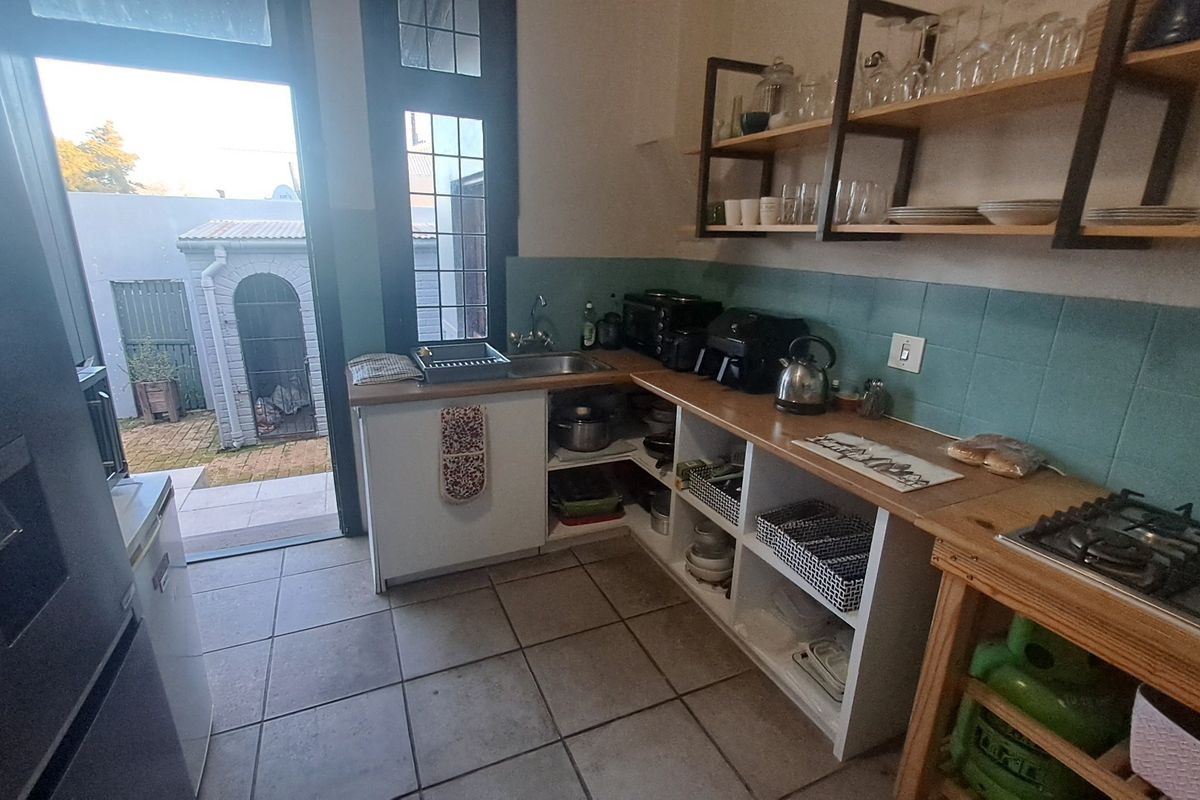 Functional kitchen featuring a gas hob, open shelving, tiled splashback, and direct access to the rear outdoor area.