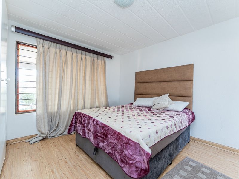 A bedroom featuring laminate flooring, a textured ceiling, and a built-in wardrobe, offering a functional space with neutral finishes.