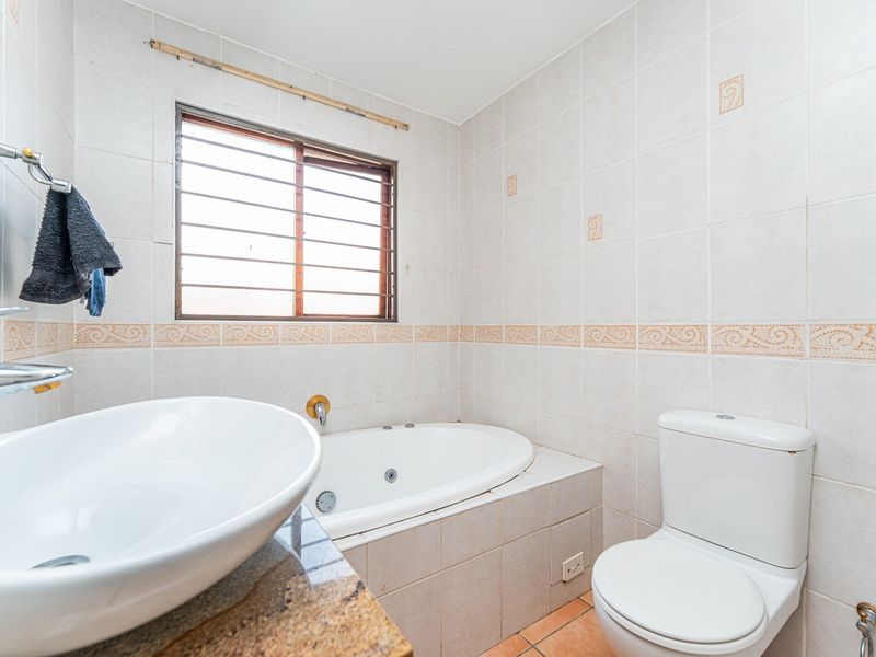 A functional bathroom featuring a built-in bathtub, granite-topped vanity, and neutral ceramic tiling throughout.