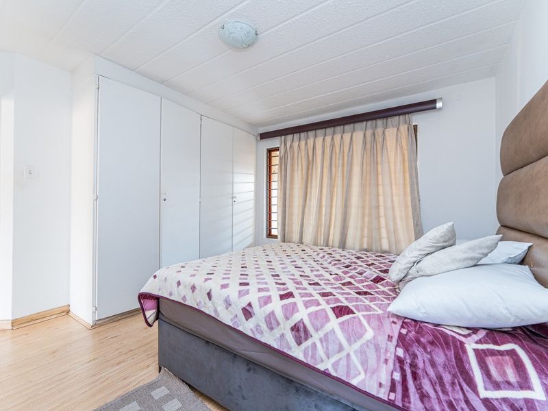 A bedroom featuring built-in cupboards, laminate flooring, and a ceiling light fixture.