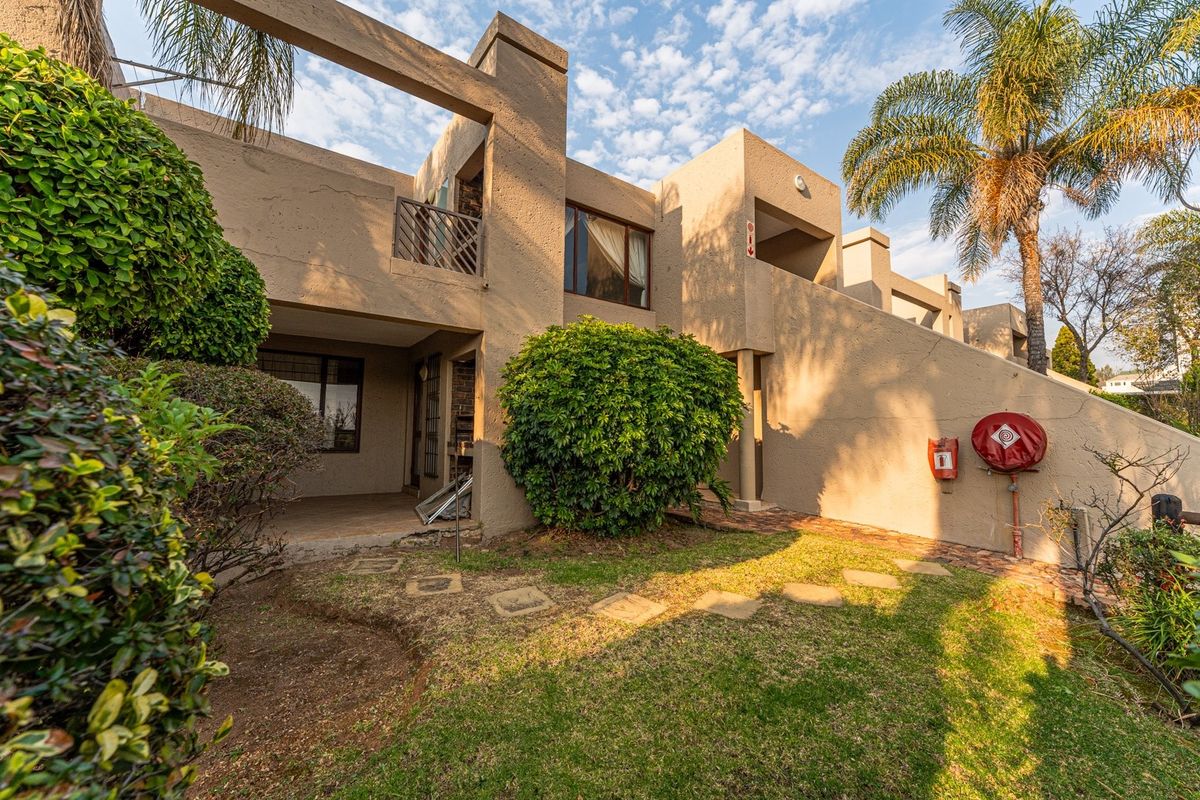 Rear view of the apartment complex featuring a private garden area, paved pathway, and balcony access with integrated fire safety equipment.