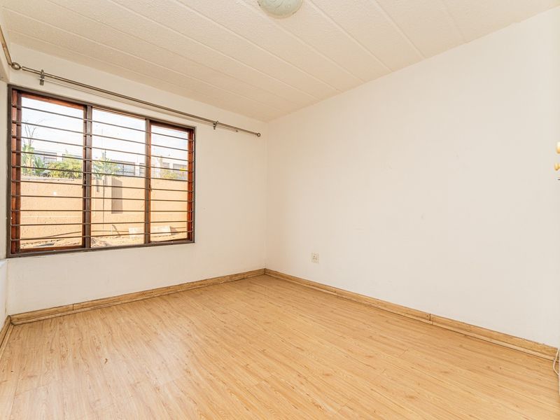 An empty bedroom featuring laminate flooring, security bars on the window, and neutral walls, providing a blank canvas for personalization.