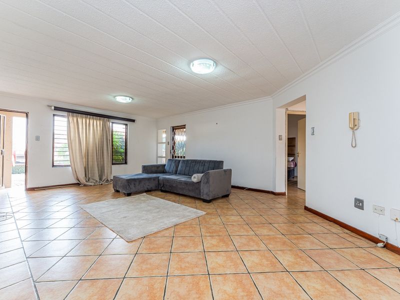 Spacious living room featuring ceramic floor tiles, security gates, and burglar bars, offering a functional layout with direct access to the exterior.