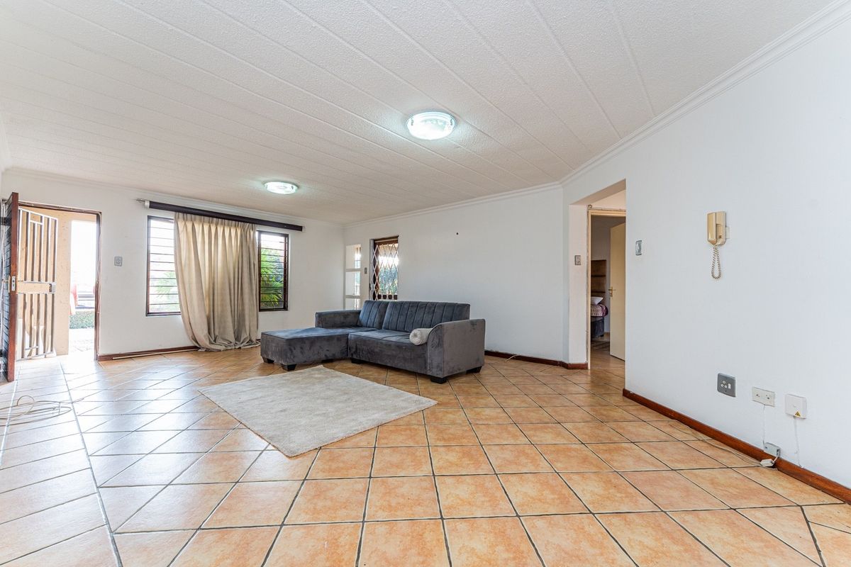 Spacious living room featuring ceramic floor tiles, security gates, and burglar bars, offering a functional layout with direct access to the exterior.