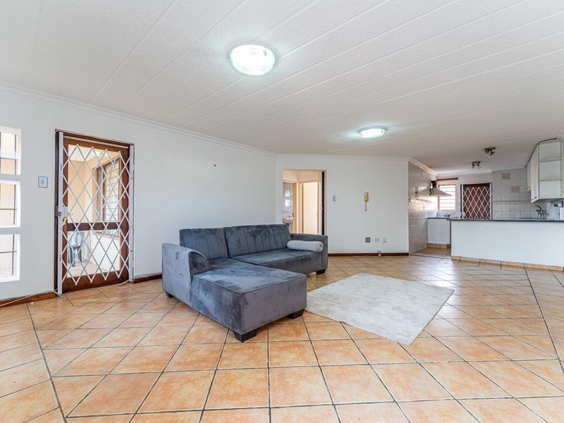 Spacious open-plan living area featuring tiled flooring, a functional kitchen with built-in cabinetry, and direct access to an external security gate.