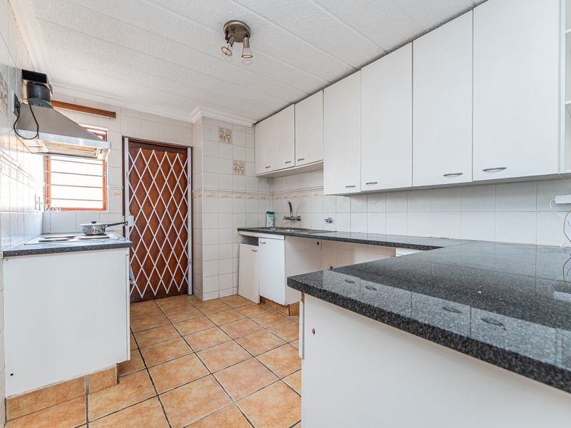A functional kitchen featuring white cabinetry, dark granite countertops, tiled backsplash, and ceramic flooring, with a security gate leading to the exterior.