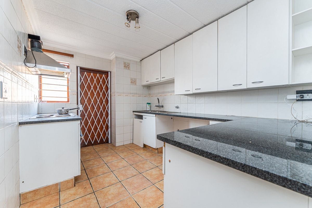 A functional kitchen featuring white cabinetry, dark granite countertops, tiled backsplash, and ceramic flooring, with a security gate leading to the exterior.