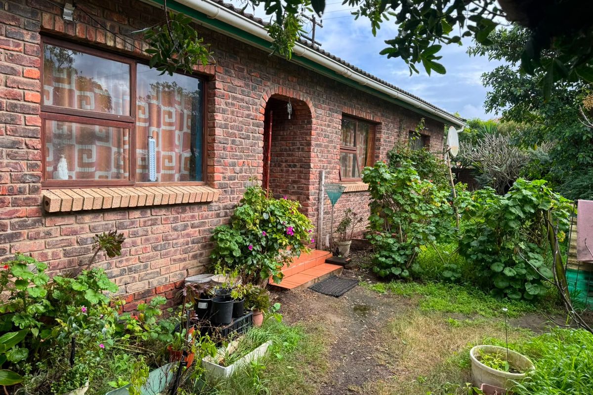 Rear exterior view of a face brick house featuring an arched entrance, tiled steps, and established garden area.