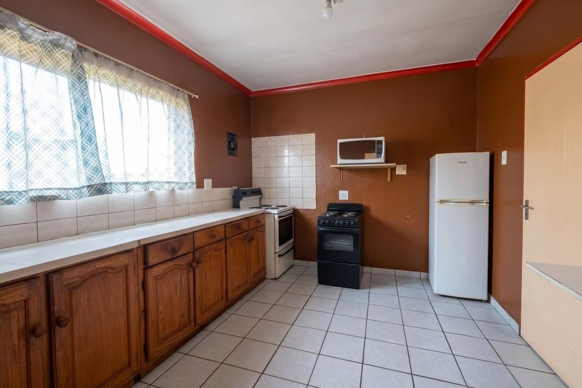 A functional kitchen featuring wooden cabinetry, tiled flooring, and a tiled splashback, offering a dated aesthetic ready for modernization.
