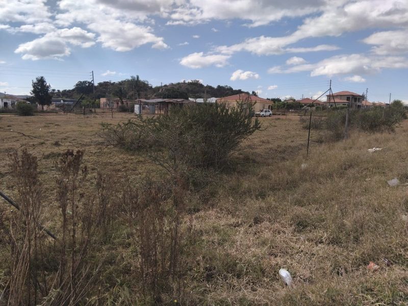 A view of a vacant residential plot featuring natural grass cover, wire fencing, and surrounding neighborhood infrastructure.