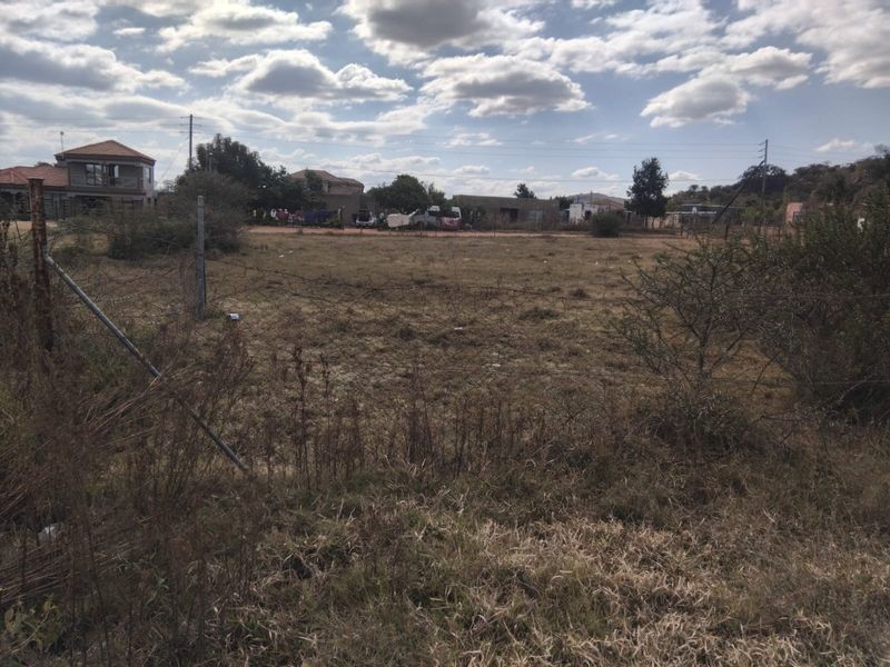 A vacant residential plot of land featuring natural grass cover and perimeter wire fencing in a suburban neighborhood setting.