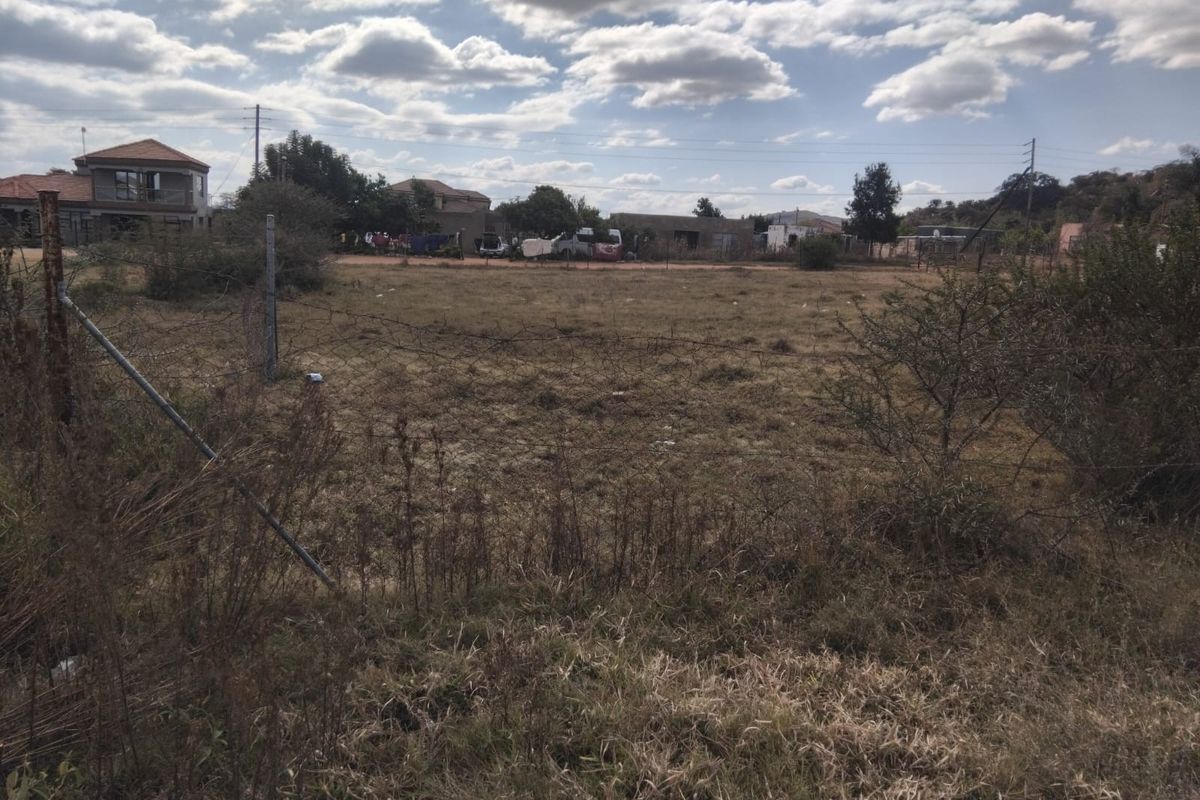 A vacant residential plot of land featuring natural grass cover and perimeter wire fencing in a suburban neighborhood setting.