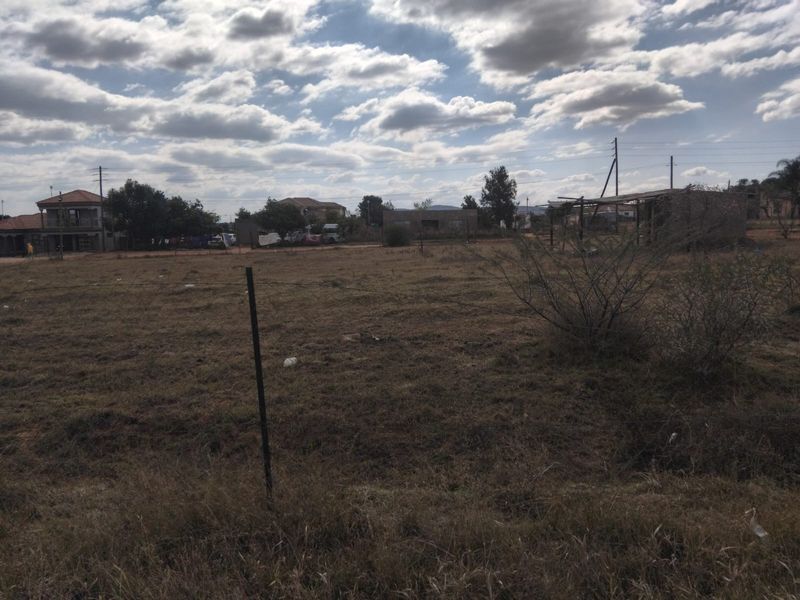 A vacant residential plot of land featuring natural grass cover and wire perimeter fencing in a suburban neighborhood setting.