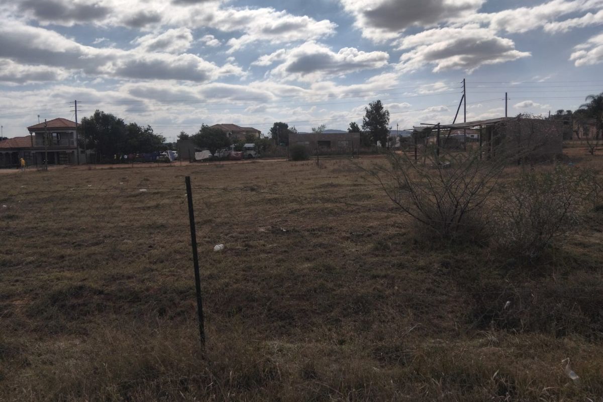 A vacant residential plot of land featuring natural grass cover and wire perimeter fencing in a suburban neighborhood setting.