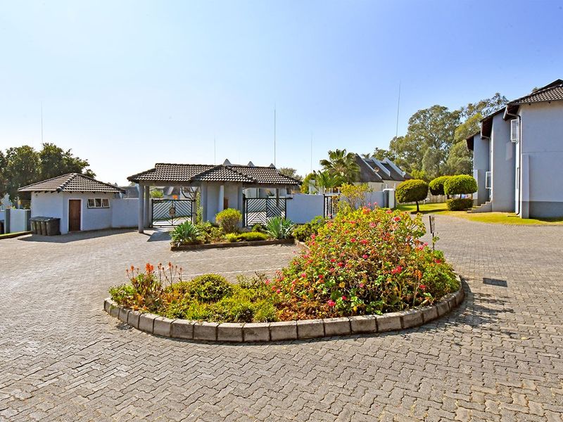 A view of the apartment complex entrance featuring a paved driveway, security gate, and a central landscaped garden bed.