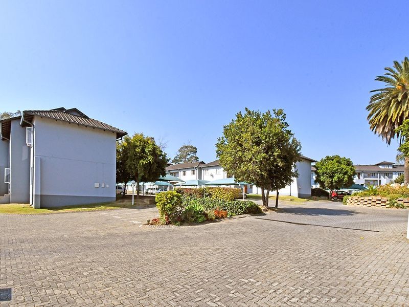 A view of the apartment complex exterior featuring paved parking areas, established landscaping, and covered parking bays under a clear blue sky.