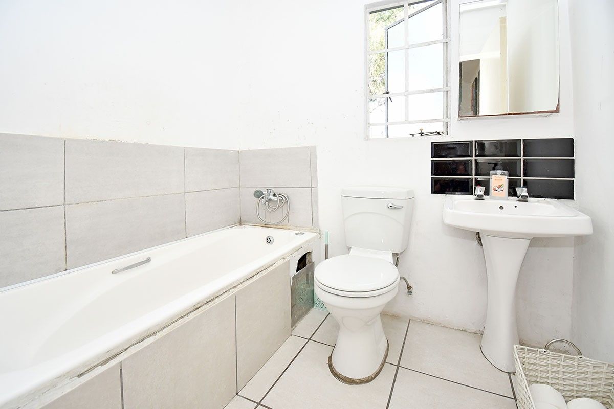 A functional bathroom featuring a bathtub, pedestal sink, and toilet, currently requiring maintenance and cosmetic updates to the tiling and wall finishes.