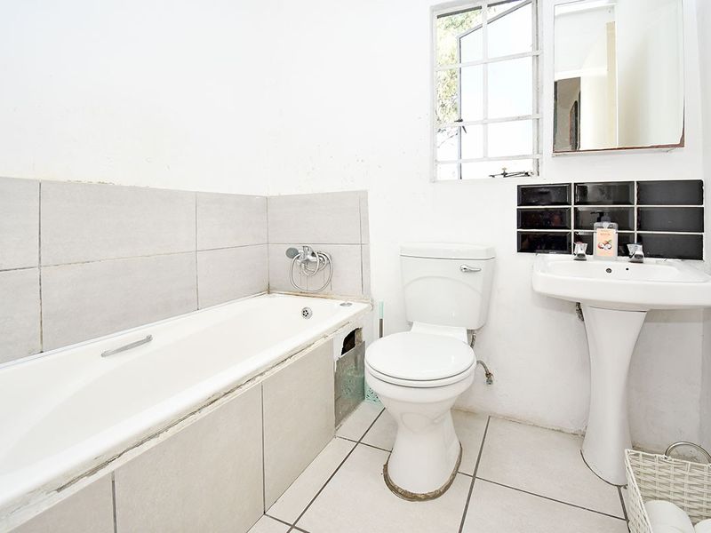 A functional bathroom featuring a bathtub, pedestal sink, and toilet, currently requiring maintenance and cosmetic updates to the tiling and wall finishes.