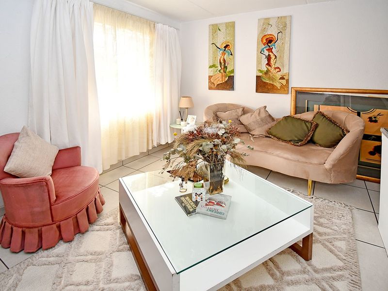 A bright living room featuring tiled flooring and large windows with curtains, providing a comfortable and well-lit space.