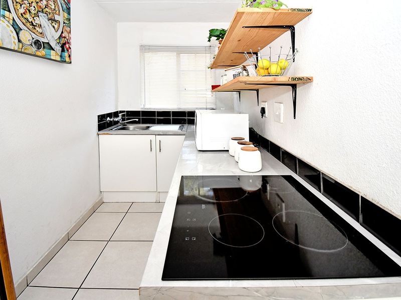 Compact kitchen featuring white cabinetry, a modern ceramic hob, tiled splashbacks, and tiled flooring, providing a functional and efficient workspace.