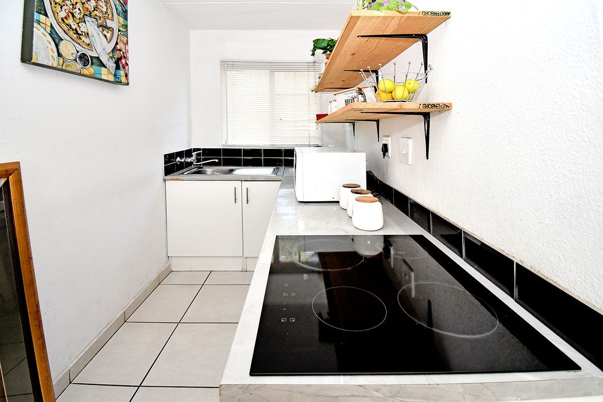 Compact kitchen featuring white cabinetry, a modern ceramic hob, tiled splashbacks, and tiled flooring, providing a functional and efficient workspace.