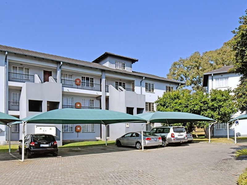 Exterior view of a multi-story apartment complex featuring paved parking areas with shade cloth carports and private balconies.