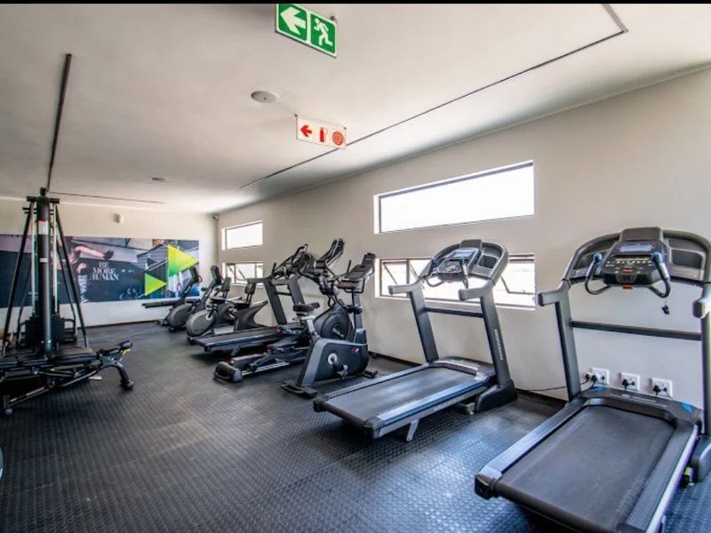 A well-maintained apartment complex gym featuring rubberized flooring, multiple treadmills, and horizontal windows providing natural light.