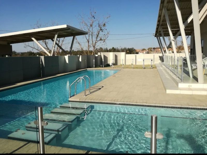 A modern outdoor pool area featuring a paved deck, glass balustrades, and a contemporary metal pergola structure.