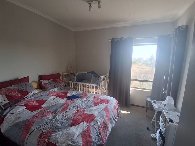 A standard bedroom featuring neutral walls, carpeted flooring, and a window with curtain rails, providing a functional living space.