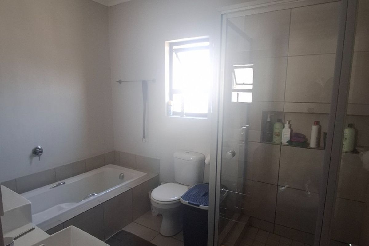 A functional bathroom featuring a built-in bathtub, separate shower enclosure, toilet, and vanity basin with neutral wall and floor tiling.