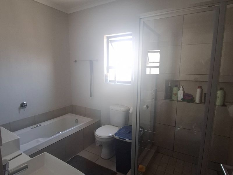 A functional bathroom featuring a built-in bathtub, separate shower enclosure, toilet, and vanity basin with neutral wall and floor tiling.