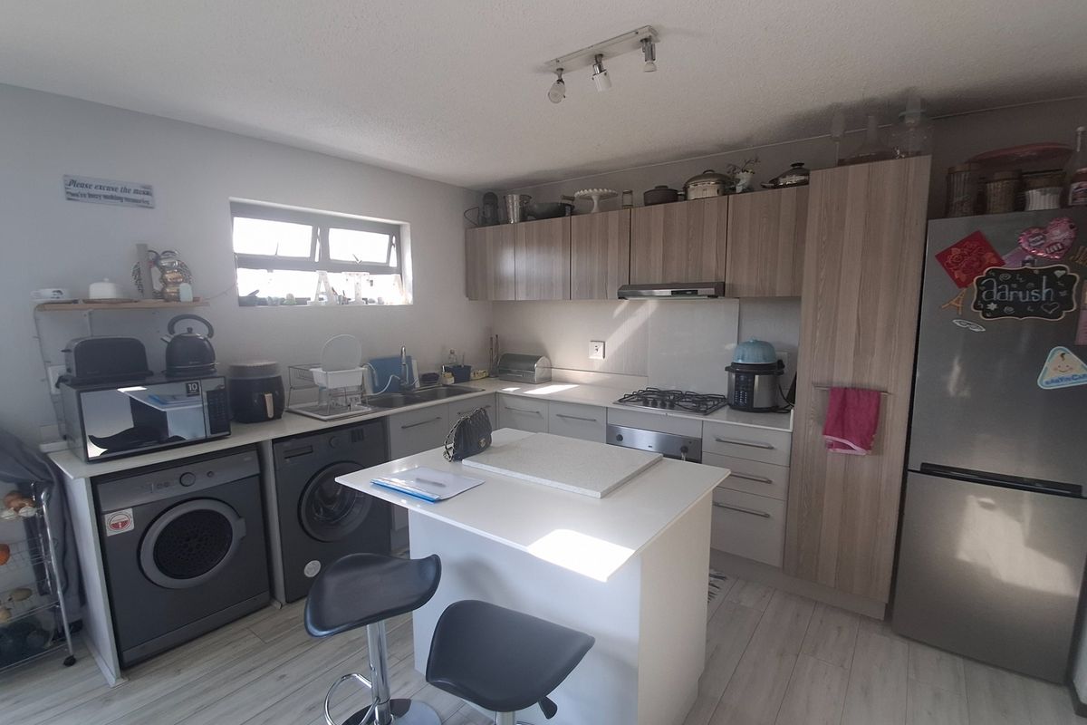 A functional kitchen featuring wood-look cabinetry, a central island, gas hob, and integrated laundry appliances, offering a practical layout for daily use.
