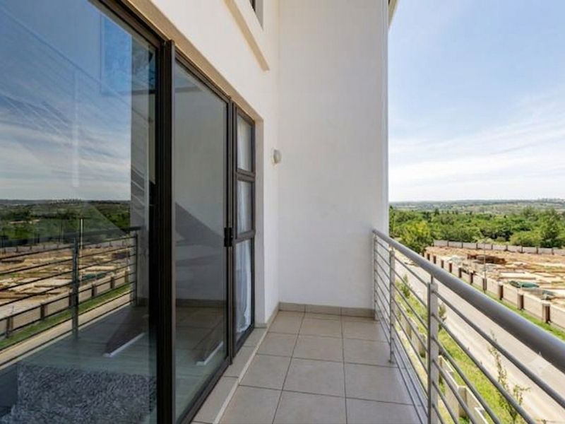 A clean, modern balcony featuring tiled flooring, a metal safety balustrade, and large sliding glass doors providing access to the interior.