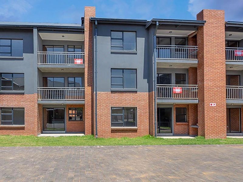 A modern multi-story apartment building featuring a combination of face brick and rendered finishes, with private balconies and paved ground-level access.